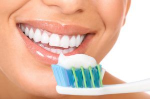 Close up of a toothbrush with toothpaste and a woman's smile in the background